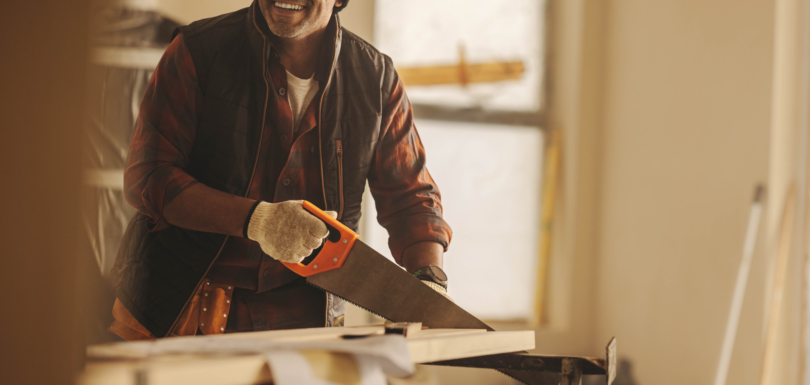Smiling contractor sawing lumber on a residential job site in DFW